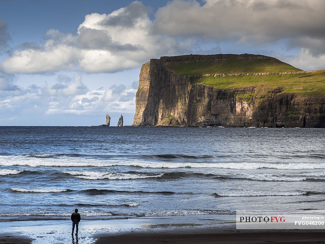 Tourist in the Tjrnuvk beach, Streymoy island. On the horizon, the silhouettes of Risin and  Kellingin sea stacks, Faeroe islands, Denmark, Europe